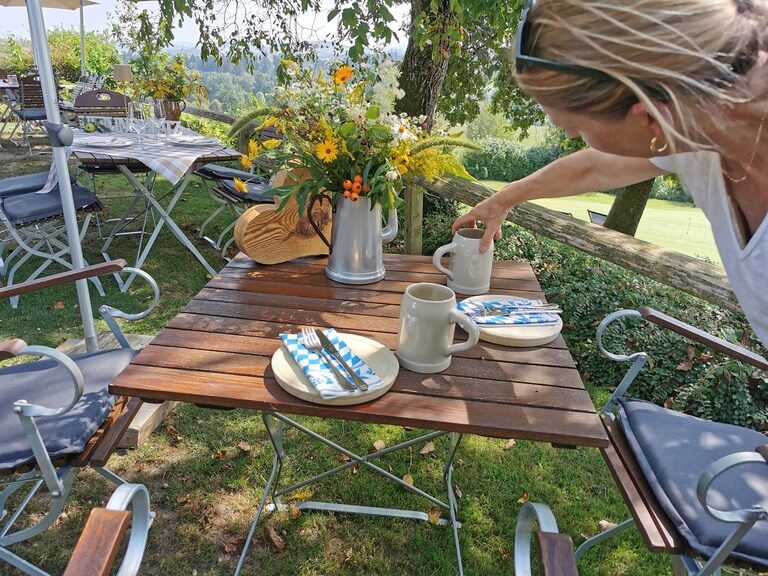 Unter strahlendem Himmel deckt eine Servicekraft im Golf- und Landhotel Anetseder einen Tisch für genussvolle Stunden im Freien.