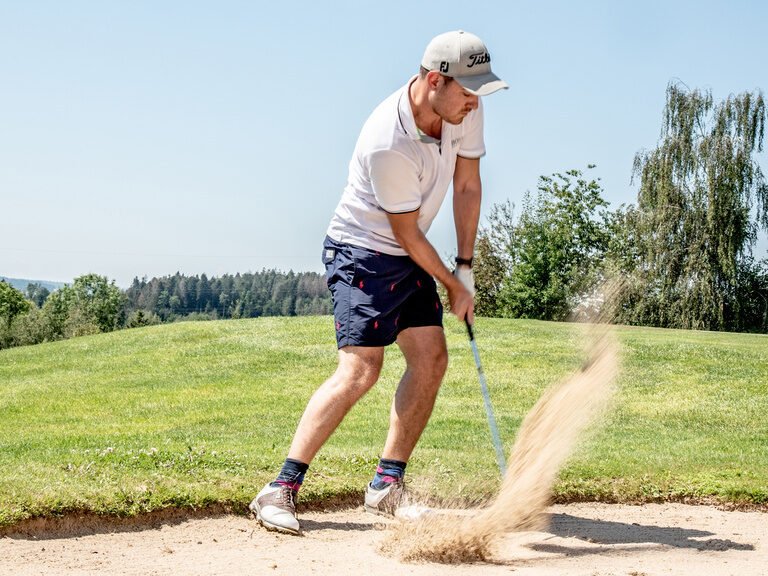 Ein Golfer schlägt den Ball aus dem Sandbunker auf das Grün der Golfanlage des Hotel Anetseder.