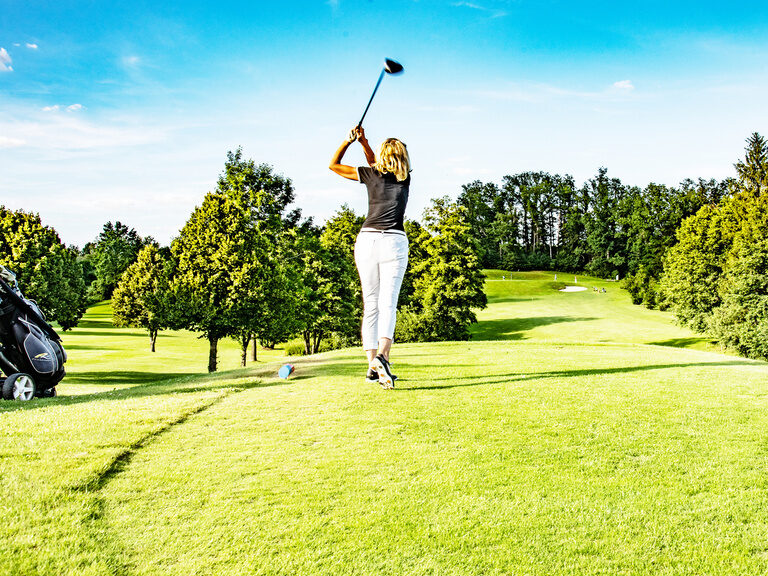 Eine Frau schlägt bei schönem Wetter motiviert einen Ball auf dem Golfplatz des Golfhotels Anetseder.