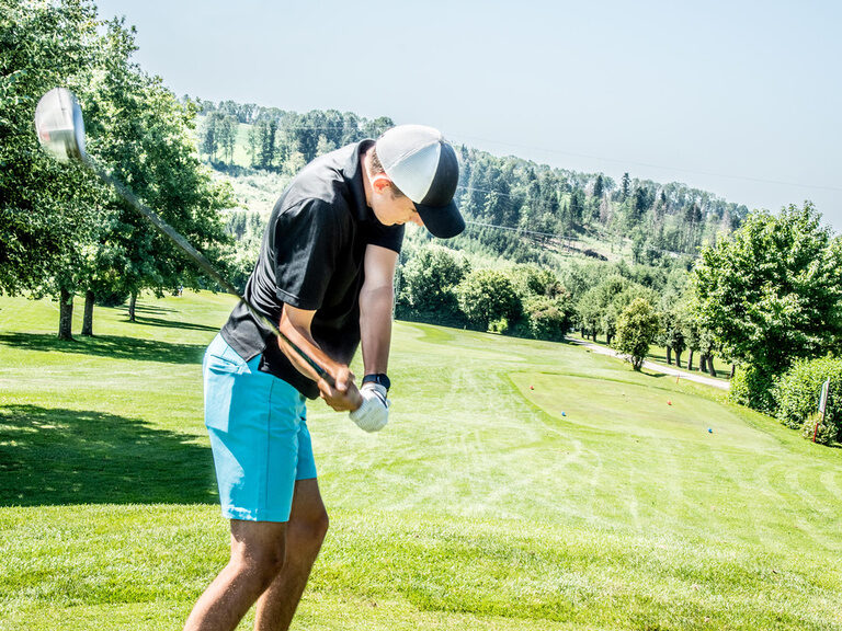 Ein junger Golfer schwingt seinen Golfschläger beim Abschlag auf der hauseigenen Golfanlage des Hotel Hotel Anetseder mustergültig durch